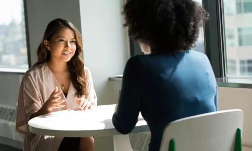 Image de 2 femmes discutant autour d'une table. Image représentant le dialogue clair nécessaire pour la négociation