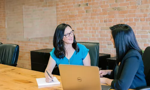 Image de 2 femmes discutant autour d'une table. Image représentant le dialogue clair nécessaire pour la négociation